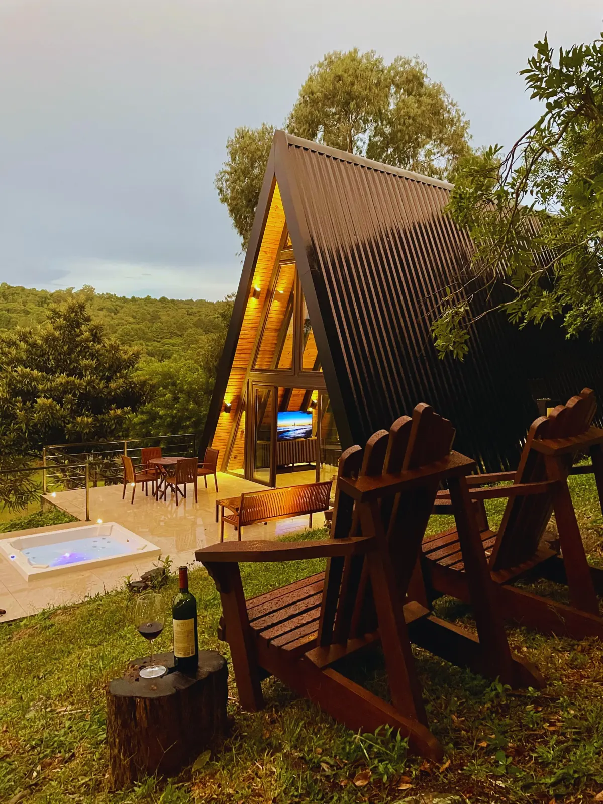 Cabana iluminada ao entardecer, jacuzzi acesa e taça de vinho junto às espreguiçadeiras