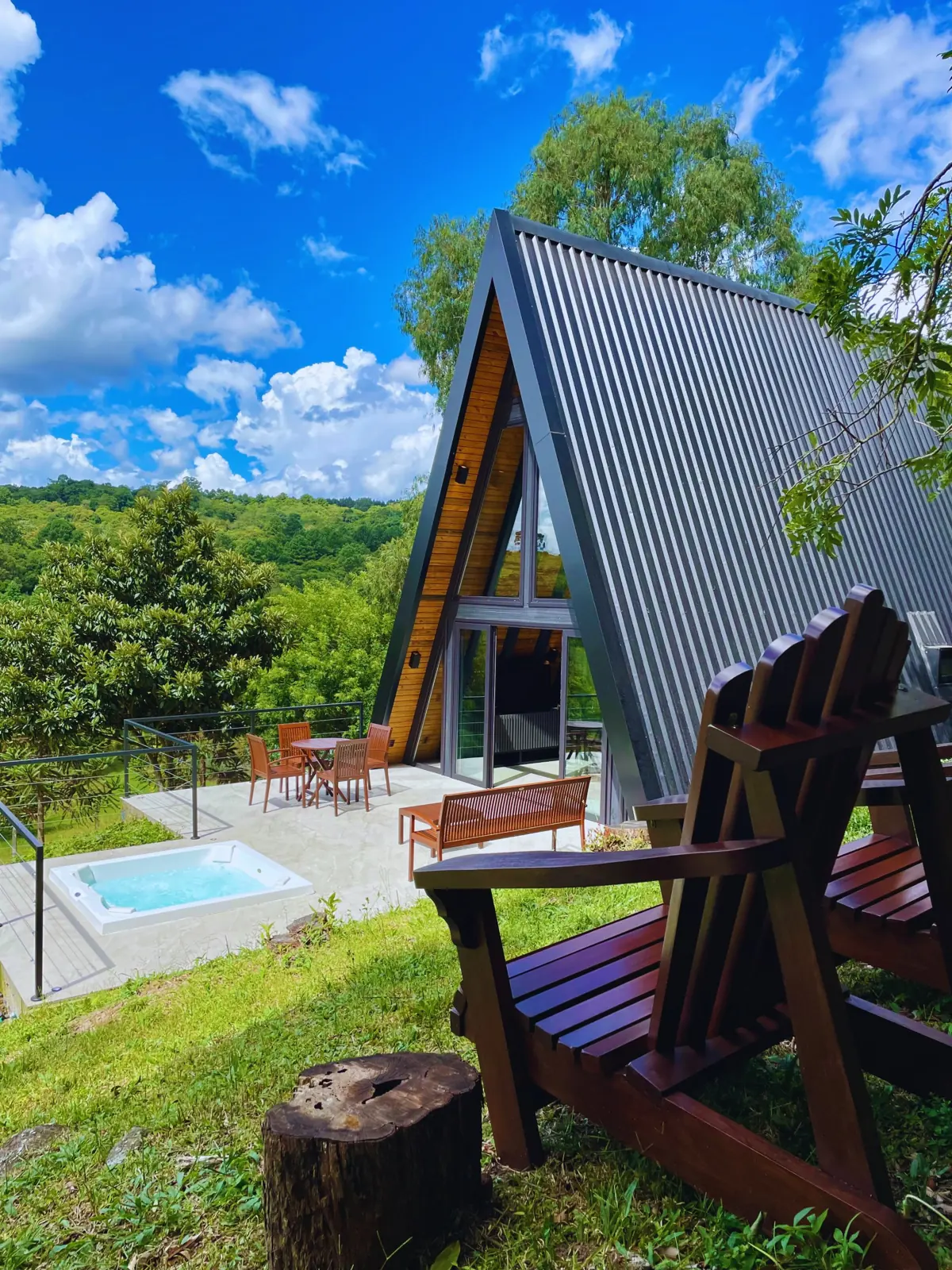 Cabana A-frame preta com deck, jacuzzi privativa e espreguiçadeiras de madeira, cercada de mata na Serra Gaúcha