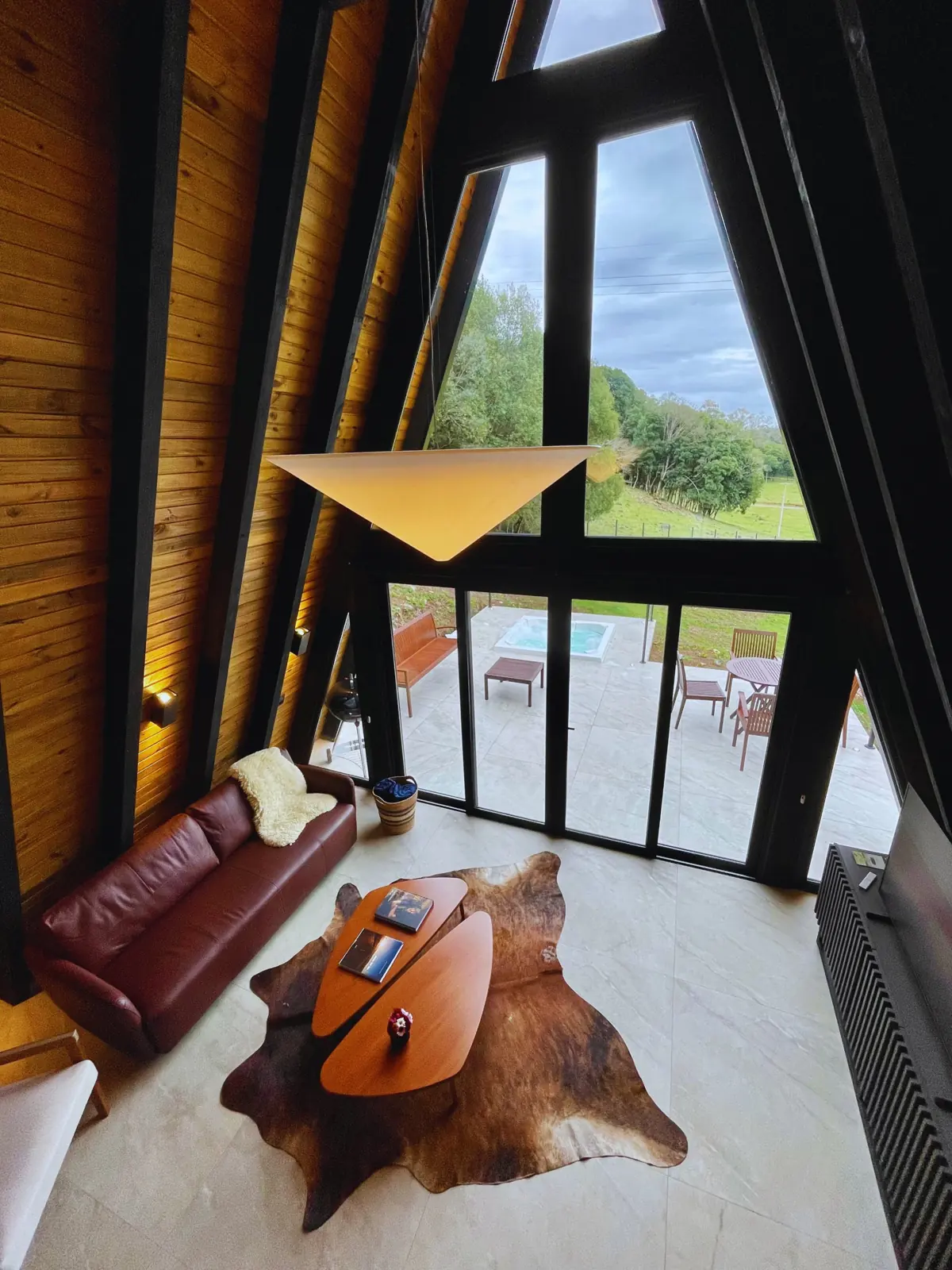 Vista do mezanino para a sala de pé-direito alto, com o deck e a jacuzzi do lado de fora