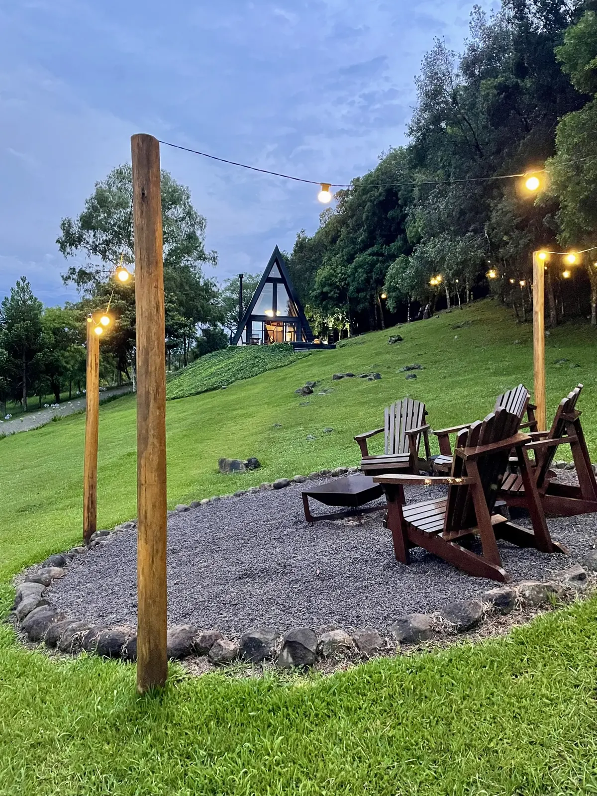 Fogueira com varal de luzes no gramado e a cabana A-frame ao fundo