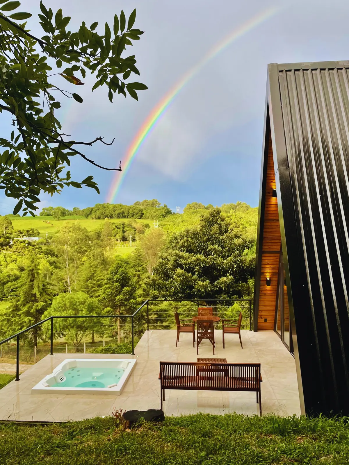 Arco-íris sobre o vale visto do deck da cabana, com a jacuzzi e a mesa externa