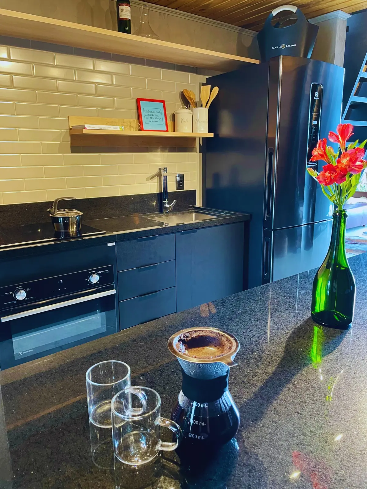 Cozinha equipada com fogão de indução, forno elétrico, micro-ondas, geladeira com freezer e café coado no balcão de granito